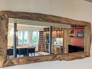 A modern kitchen with wooden accents, a dining area with a table and chairs, and a large mirror with a rustic frame. - Val Signina 6-7 by Interhome (Laax)