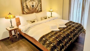 Una cama bien tendida con sábanas blancas, un cuadro con temática de lobo encima y dos lámparas de noche.