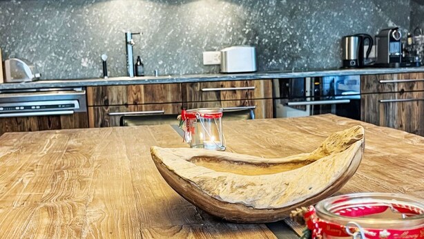 Una mesa de comedor de madera con un candelabro de vidrio y una vela, una cocina rústica con armarios de madera y electrodomésticos modernos al fondo.