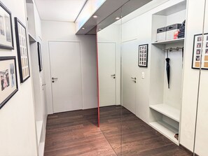 A modern hallway with wooden flooring, white walls, and a glass partition. There are framed photos on the walls and a coat rack with an umbrella. - Val Signina 6-7 by Interhome (Laax)