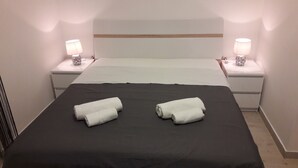 Ein Hotelzimmer mit einem Bett, zwei Nachttischlampen und zwei zusammengerollten Handtüchern auf dem Bett.