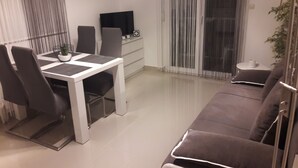 Ein modernes Wohnzimmer mit einer Couch, einem Esstisch mit Stühlen, einem Fernseher und einer Pflanze.