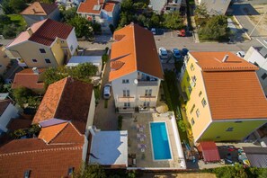 A residential area with a swimming pool, multiple buildings with red-tiled roofs, and a clear sky. - Batur Pool Apartment A4, Zadar, Croatia (Zadar)
