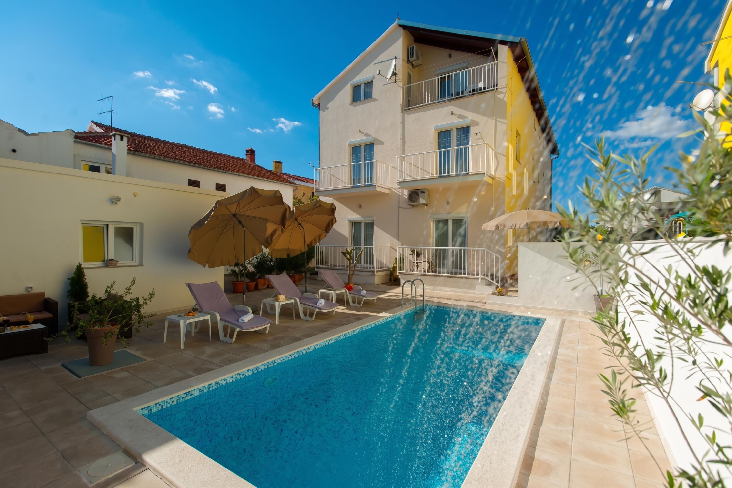 A swimming pool with lounge chairs and umbrellas, surrounded by a building with balconies.