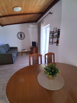 Un salon avec un plafond en bois, une table de salle à manger ronde entourée de chaises, un canapé, un téléviseur et une horloge murale.