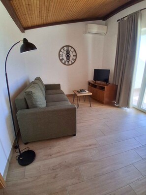 A living room with a sofa, a TV, a clock, and a lamp.