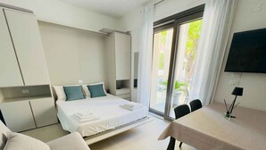 A modern hotel room with a bed, a sofa, a dining table, and a TV. - Studio with air conditioning, balcony and internet (Pesaro)