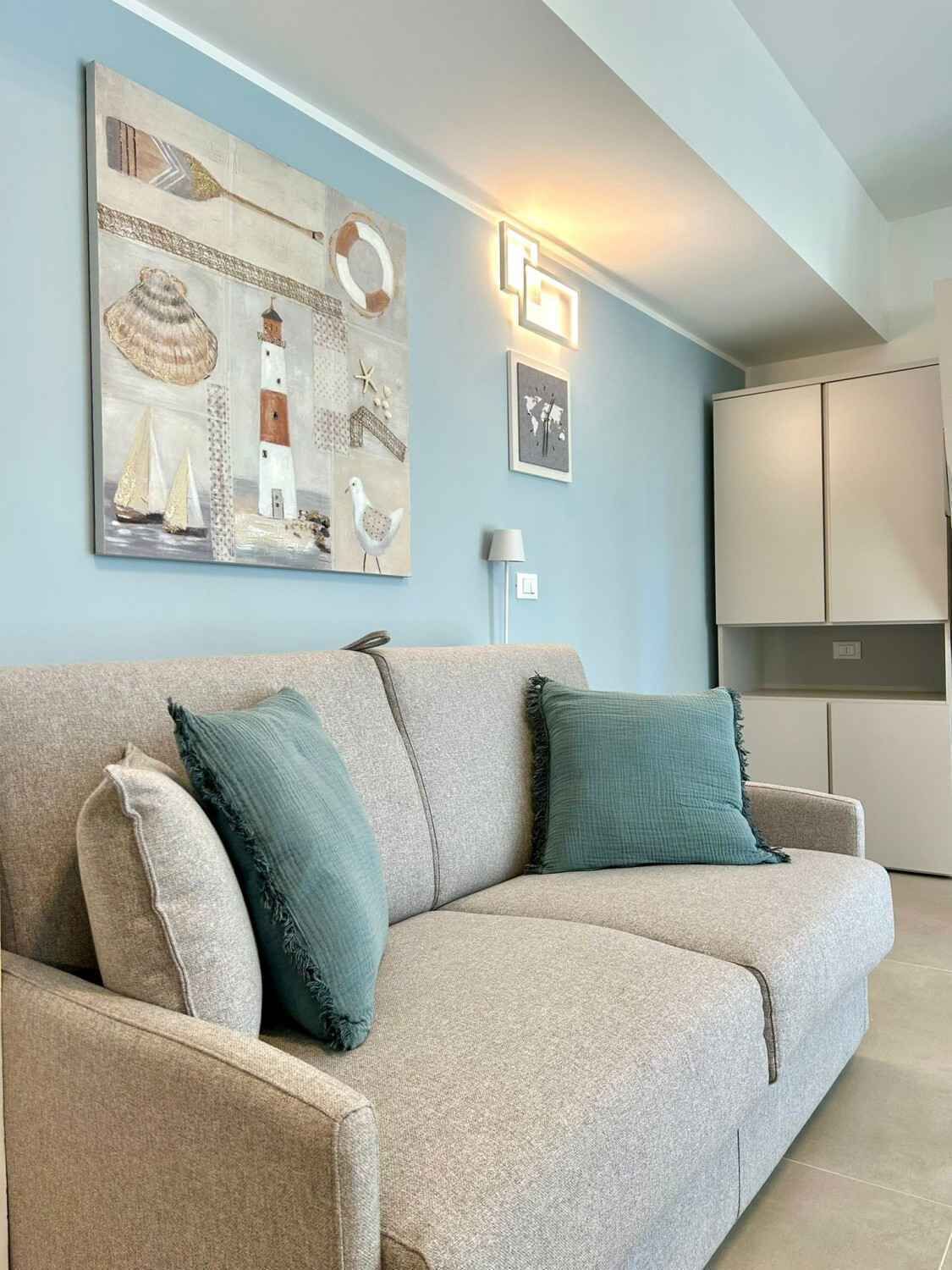 A living room with a sofa, cushions, a painting, a lamp, and a wardrobe.