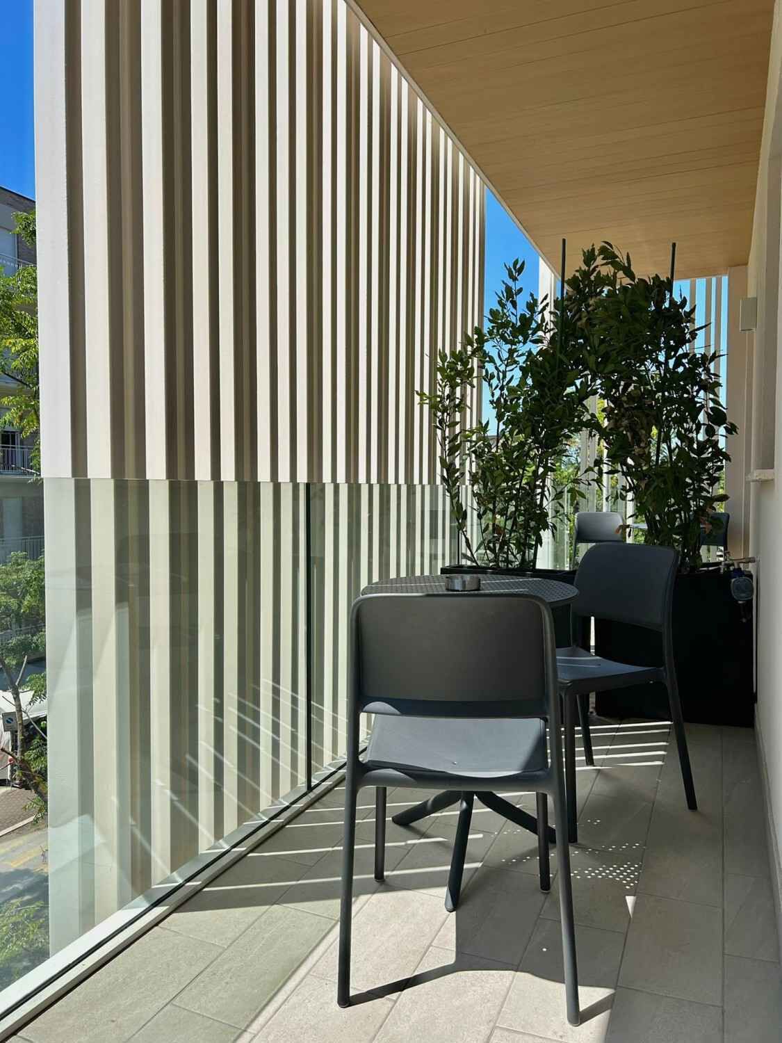 Ein Balkon mit modernem Design, der vertikale Linien an der Wand, eine Glasbrüstung und zwei Stühle zeigt.