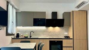 A modern kitchen with built-in appliances, a dining area with chairs, and a flat-screen TV mounted on the wall. - Studio with air conditioning, balcony and internet (Pesaro)