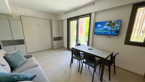 A modern kitchen with a dining area, a sofa, and a TV on the wall. - Studio with air conditioning, balcony and internet (Pesaro)