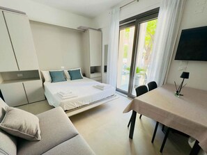 Ein modernes Hotelzimmer mit Bett, Sofa, Esstisch und Fernseher.