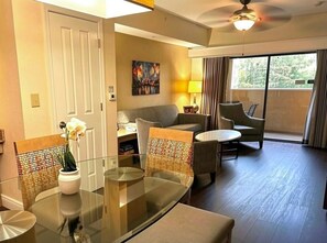 A hotel room with a glass dining table, cushioned chairs, a sofa, a ceiling fan, and a view of the outdoors. - Resort Condo for 8 Guests just minutes to Disney! (Orlando)