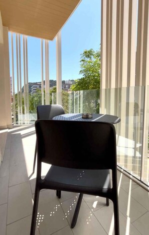 A balcony with a chair and table, large windows, and a view of buildings and trees. - Holiday apartment with air conditioning, balcony and internet (Pesaro)