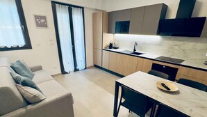 Una cuina moderna amb forn integrat, zona menjador amb taula i cadires, i sofà a la sala d'estar.