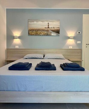 A bedroom with a bed, two bedside lamps, a wall-mounted picture, and folded towels on the bed. - Holiday apartment with air conditioning, balcony and internet (Pesaro)