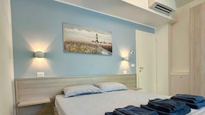 Un dormitori amb llit, dues làmpades de nit, un quadre, un aparell d'aire condicionat i una porta.