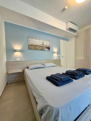 A bedroom with a bed, two bedside lamps, a painting, an air conditioning unit, and a door. - Holiday apartment with air conditioning, balcony and internet (Pesaro)