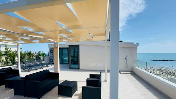 Terrassa al terrat amb seients exteriors, entrada per una porta de vidre i vista al mar.