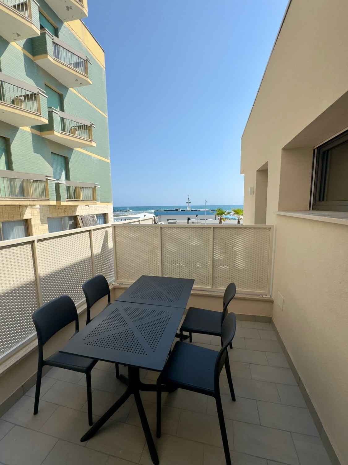 A balcony with a table and chairs, a view of the sea, and a building with balconies.