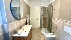 Une salle de bain moderne avec un meuble-lavabo en bois, un miroir rond, une cabine de douche en verre et des toilettes séparées.