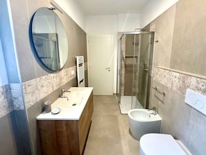 Ein modernes Badezimmer mit einem Holzbadezimmerunterschrank, einem runden Spiegel, einer Duschkabine aus Glas und einer separaten Toilette.