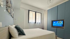 Une chambre à coucher avec un lit, un téléviseur fixé au mur, une fenêtre avec des rideaux et un luminaire au plafond.