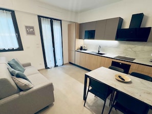 Eine moderne Küche mit integriertem Backofen, ein Essbereich mit Tisch und Stühlen sowie eine Sitzecke mit einer Couch.