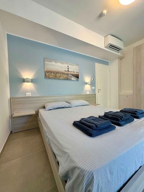 Ein Schlafzimmer mit einem Bett, zwei Nachttischlampen, einem Gemälde, einer Klimaanlage und einer Tür.