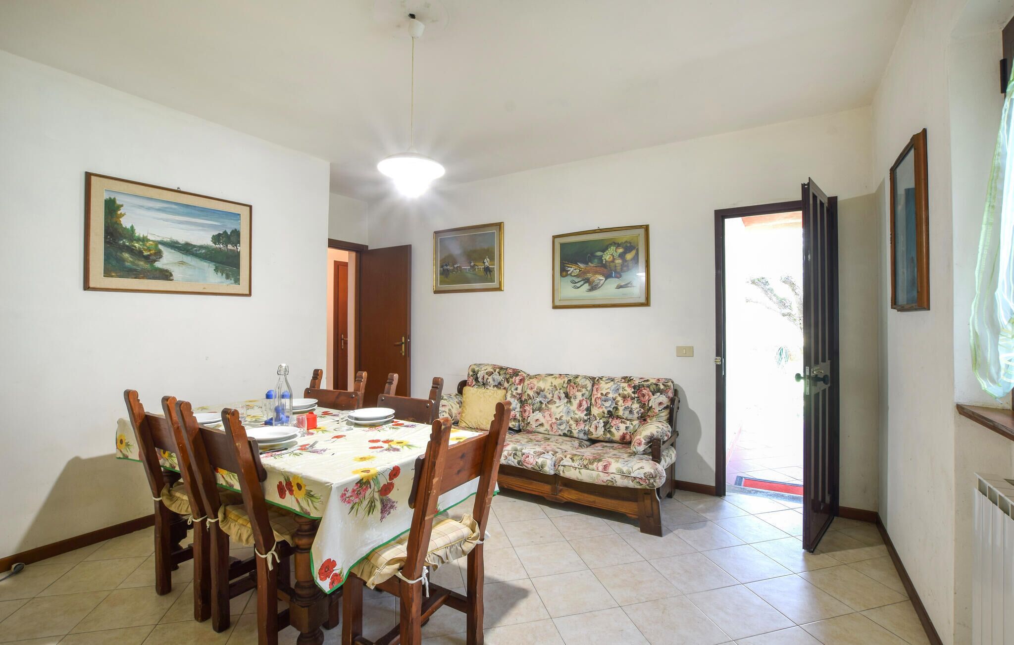 A dining area with a table set for four, a floral sofa, and three framed paintings on the walls.
