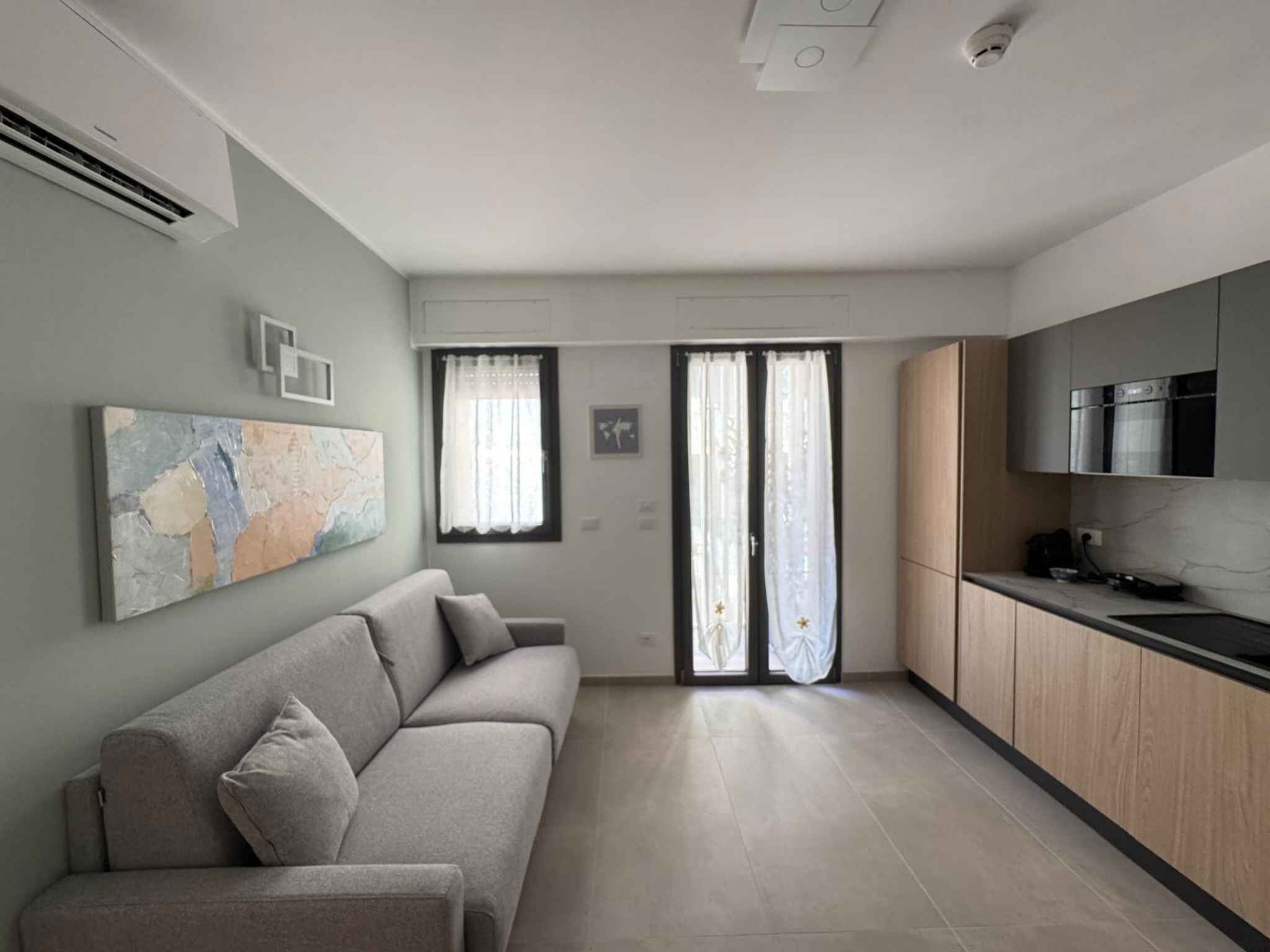 Una cuina moderna amb forn integrat i microones, un sofà gris amb coixins, i un mapa a la paret.