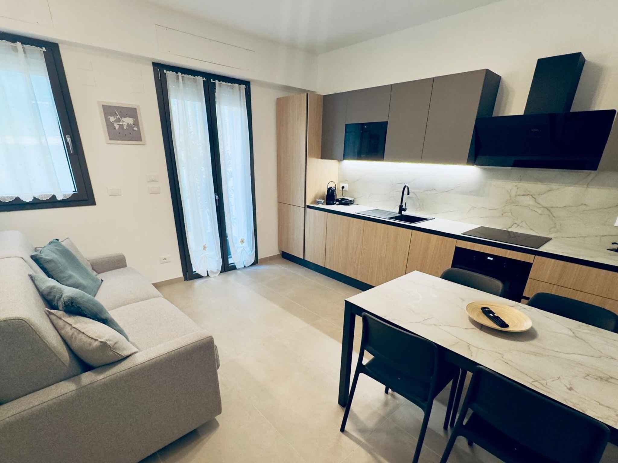A modern kitchen with a built-in oven, a dining area with a table and chairs, and a sofa in a living area.