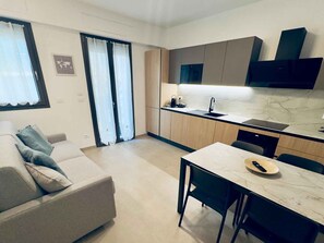 Eine moderne Küche mit integriertem Backofen, ein Essbereich mit Tisch und Stühlen sowie eine Sitzecke mit einer Couch.