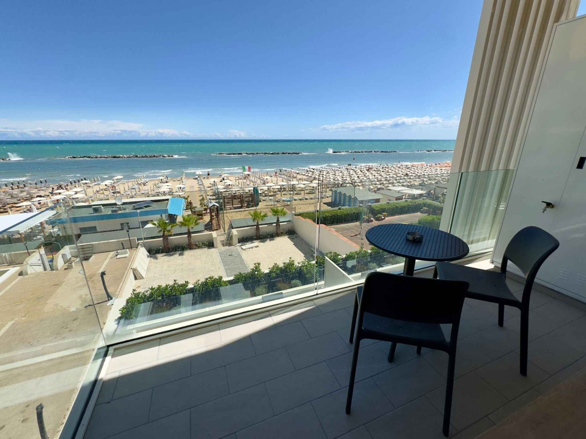 A balcony with a view of a beach, a pool, and a cityscape.