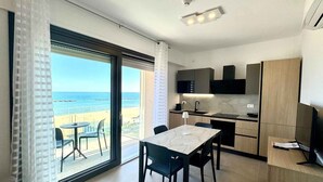 Quarto moderno com área de refeições, cozinha e uma grande porta de vidro deslizante com vista para a praia.