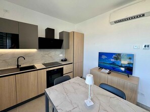 A modern kitchen with a built-in stove, a sink, and a flat-screen TV on a wooden stand. - Holiday apartment with air conditioning, internet and balcony with sea view (Pesaro)