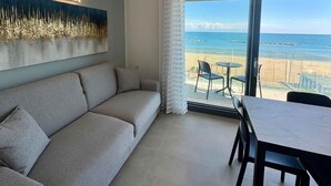 Quarto moderno com sofá, mesa de jantar e vista para a praia.