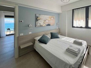 Ein Schlafzimmer mit einem Bett, zwei Kissen, einem Nachttisch, einer Wandleuchte und einem Fenster mit Vorhängen.