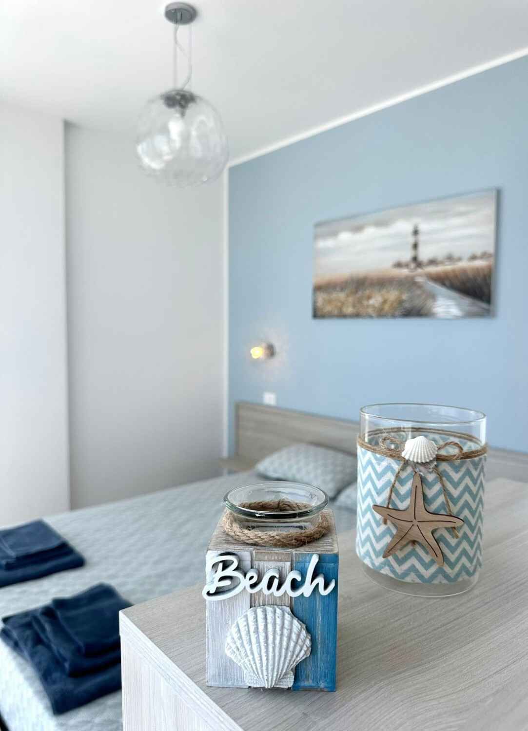 Une chambre à coucher avec un lit, une table de chevet, une lampe, un tableau, un vase décoratif et une bougie.