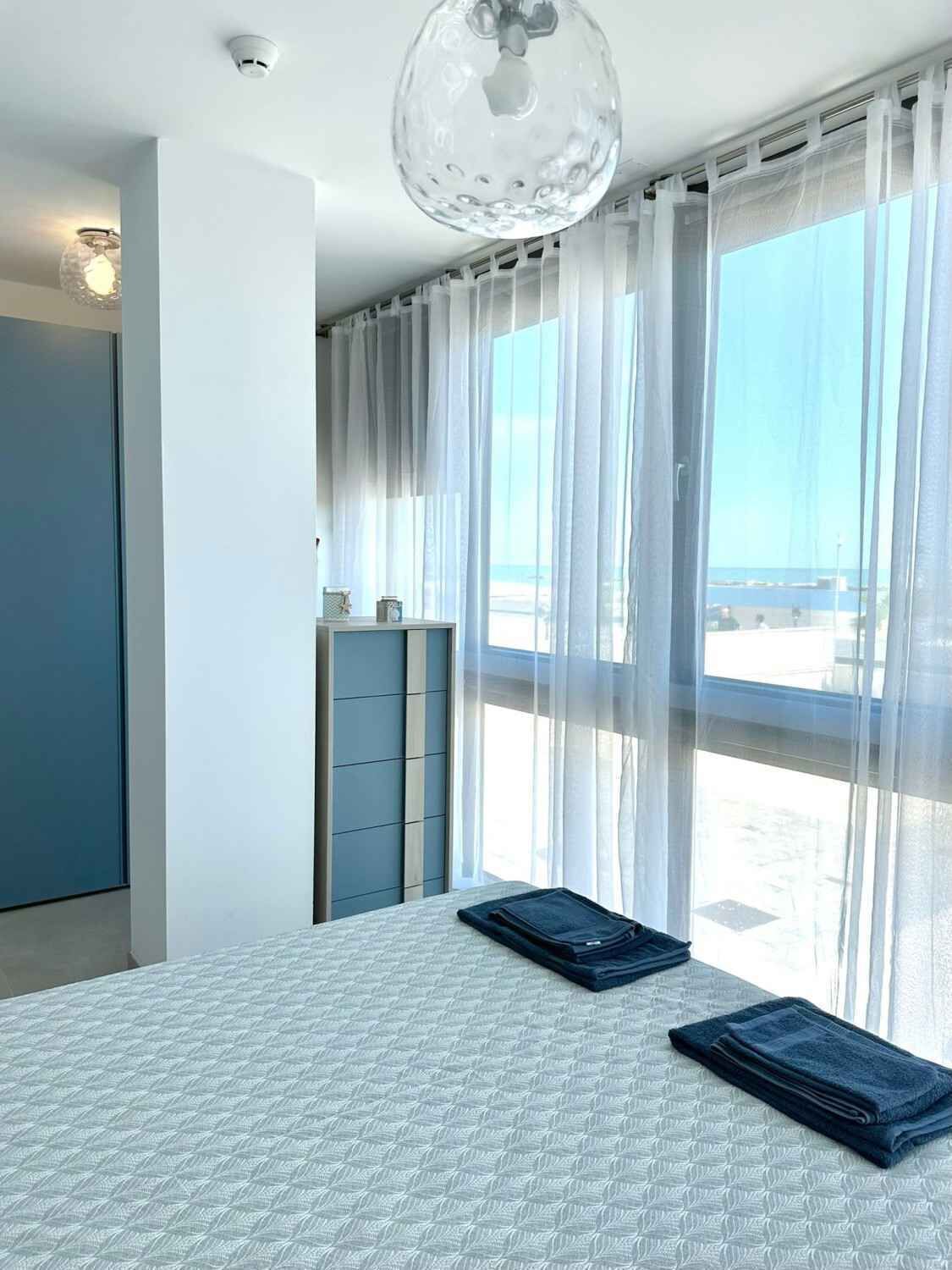 Een moderne slaapkamer met een groot bed, een dressoir en lichte gordijnen.