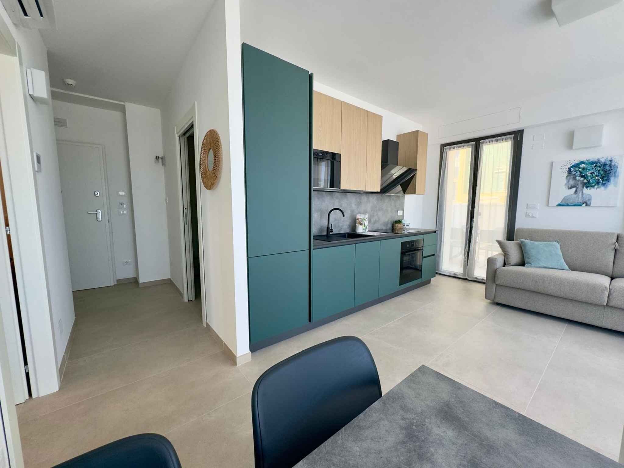 Cozinha moderna com armários verde-água, sala de jantar com mesa e cadeiras, e sala de estar com sofá e um quadro.
