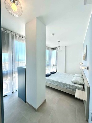 A modern bedroom with a bed, a hanging light fixture, and a view through a window. - Holiday apartment with air conditioning, internet and balcony with sea view (Pesaro)