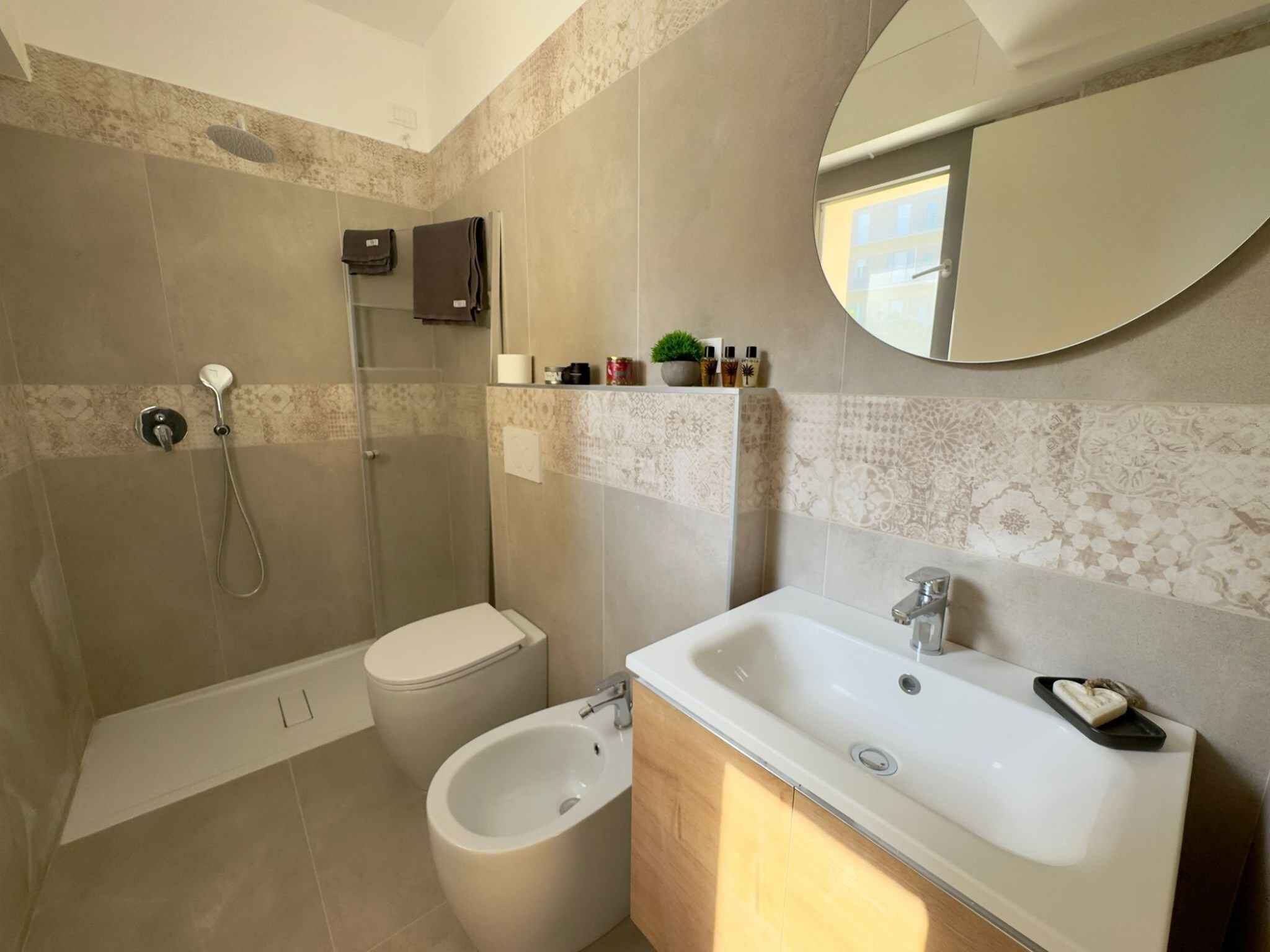 Un bany modern amb dutxa, vàter, bidet i un gran lavabo amb mirall.