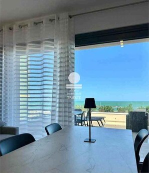 Ein Zimmer mit Tisch, Stühlen, einer Lampe und Blick auf den Ozean.