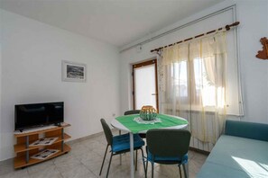 A dining area with a table, chairs, a television on a stand, and a window with curtains. - Holiday Apartment Mary with Air Conditioning (Punat)