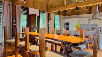 Un vaste espace dédié à la salle à manger, avec une longue table en bois et des chaises, une cuisine en arrière-plan et un plafond au style rustique.