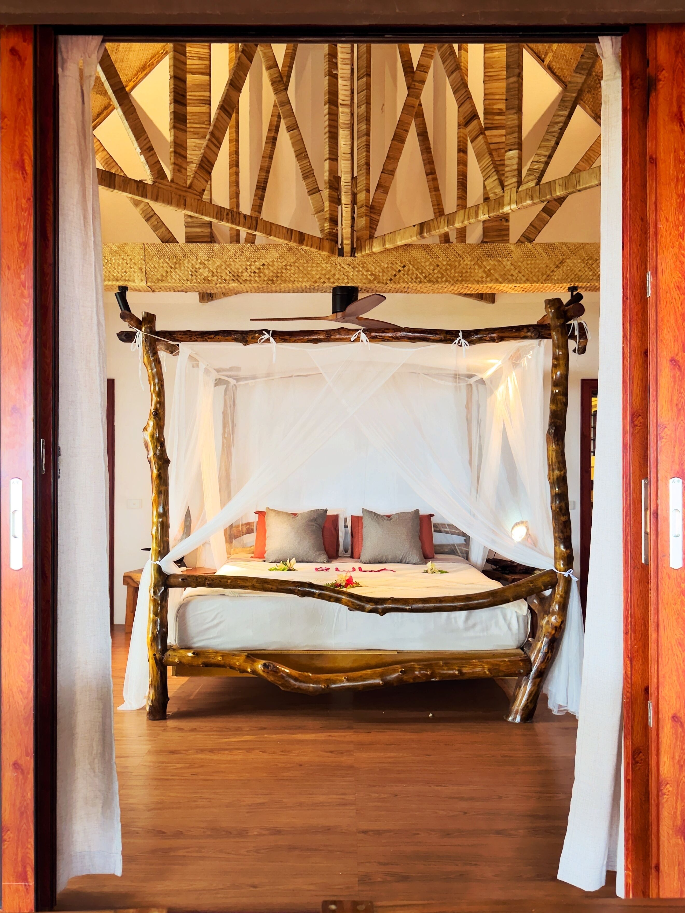A bed with a canopy, wooden beams on the ceiling, and a wooden floor.