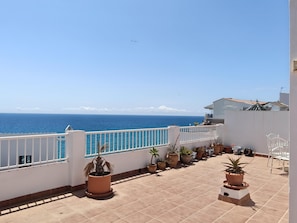 Ein Balkon mit Blumentöpfen, einem weißen Geländer und Blick aufs Meer.