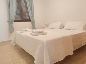 A neatly made bed with white linens and towels, a bedside table with a lamp, and a window with curtains. - Nerja Sun Apartments Carabeo Sea (Nerja)