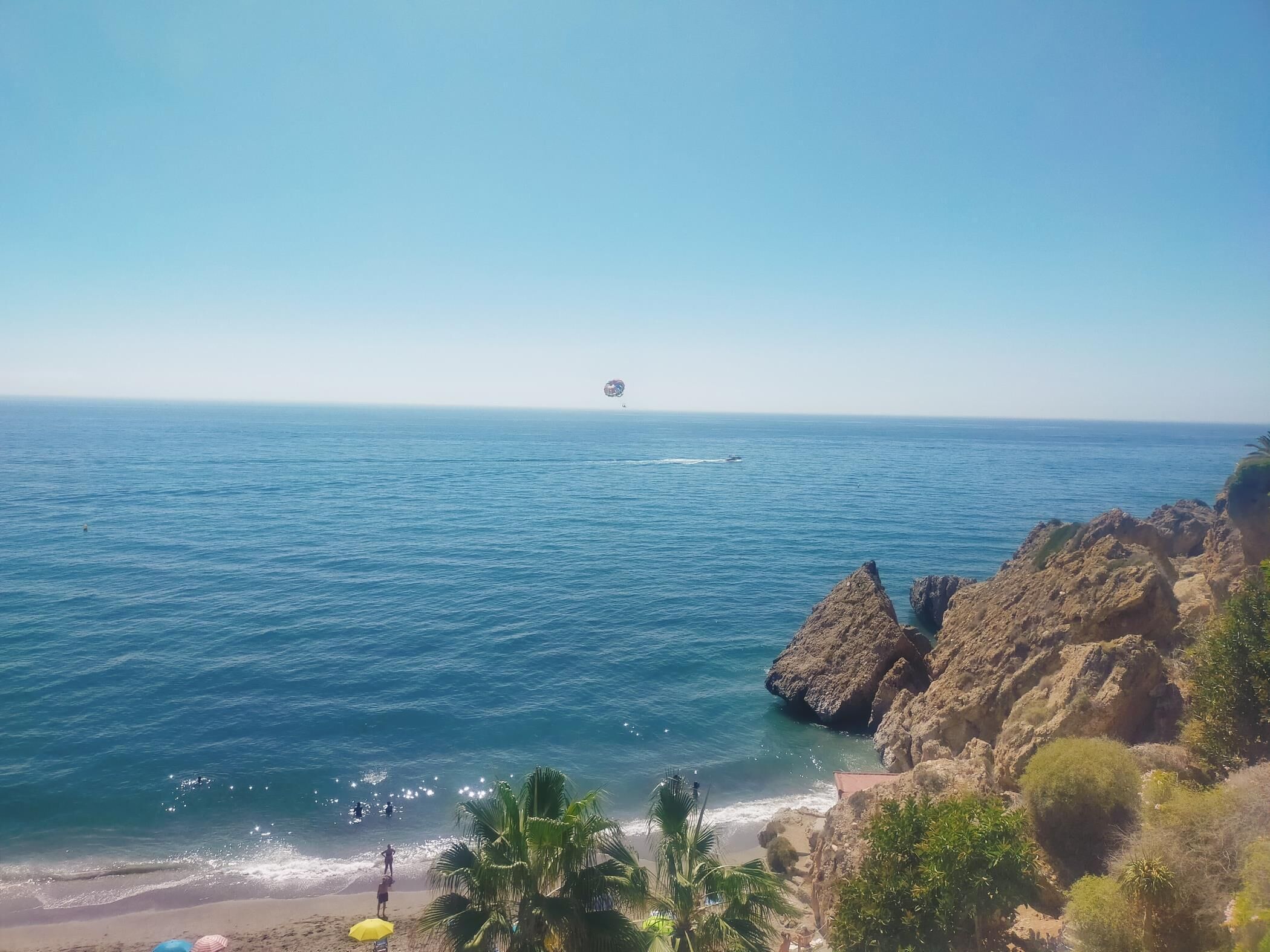 A coastal view with rocky cliffs, a beach, and a clear sky.